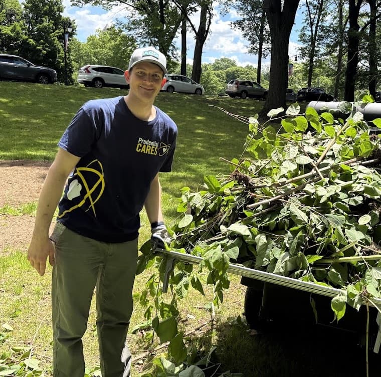 Jonah volunteering outdoors in a Prudential CARES shirt beside a cart of cleared branches